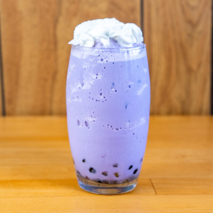 A vibrant purple taro bubble tea with whipped cream on top, against a wooden background.