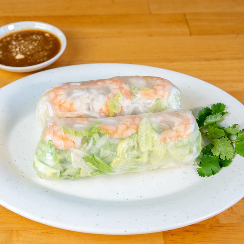 Two fresh Vietnamese spring rolls with shrimp and lettuce, served with a side of peanut sauce.