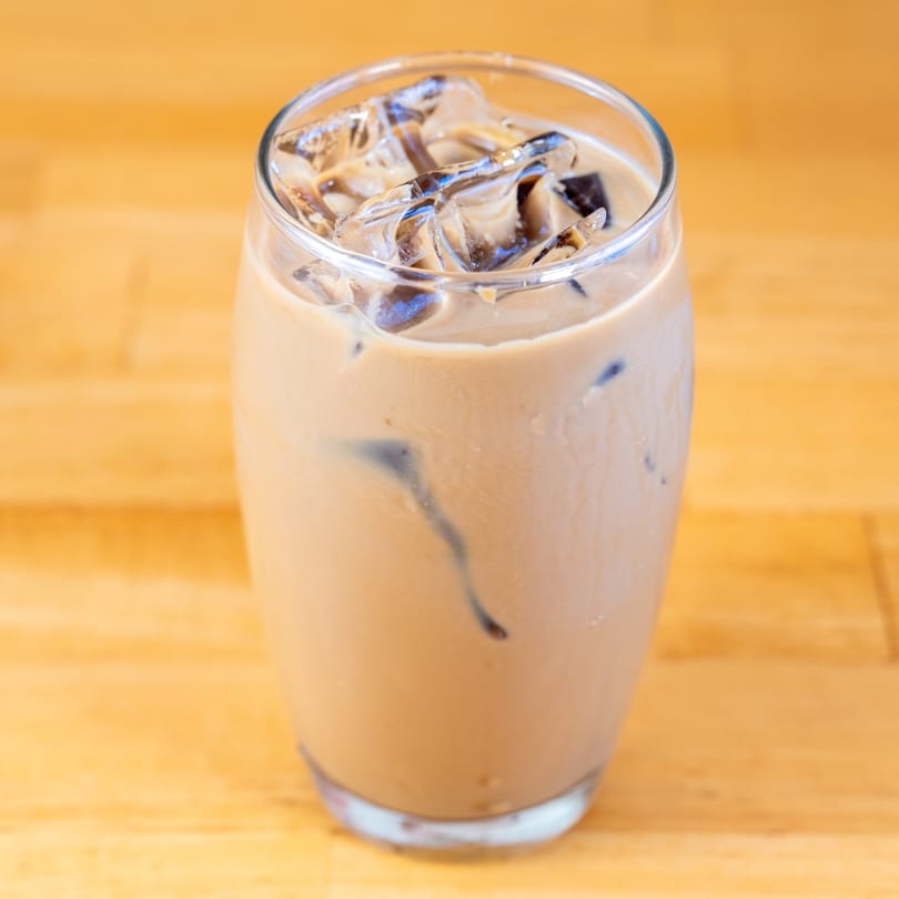 A glass of Vietnamese iced coffee with ice cubes on a light wooden table.