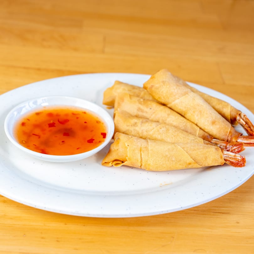 Crispy fried shrimp spring rolls with sweet chili dipping sauce on a white plate.