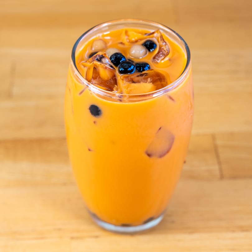 A vibrant orange Thai iced tea with ice, black boba, and white tapioca pearls in a clear glass.
