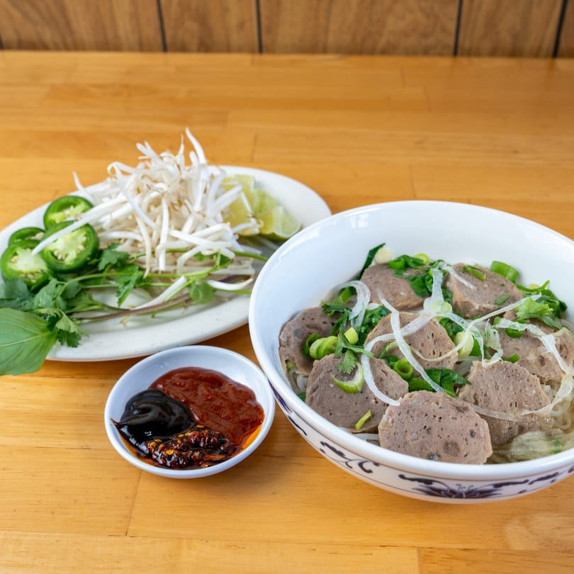 Pho Le's Vietnamese pho with sliced beef, noodles, and fresh herbs on a wooden table.